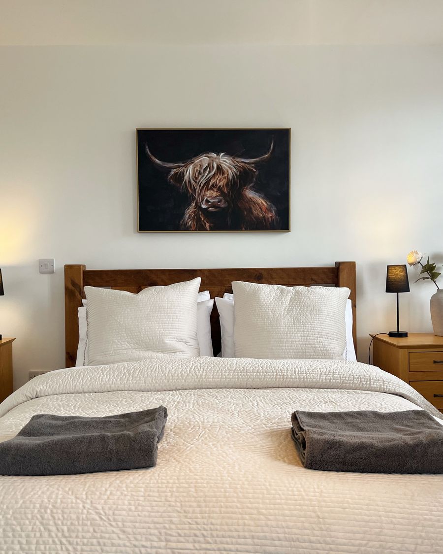 Main bedroom in the two bedroom duplex, with a wooden bedstead, fresh white linen and folded towels