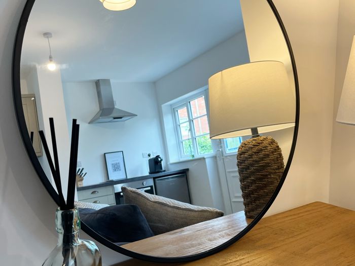 Round black mirror above an oak console with a reed diffuser