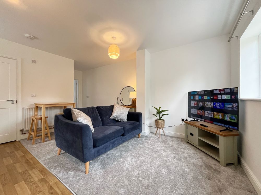 Living area of the one bedroom first floor apartment, with a navy sofa, breakfast bar and television