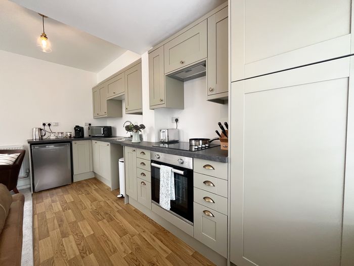 Galley kitchen with sage cabinets, oven, hob, microwave and coffee machine
