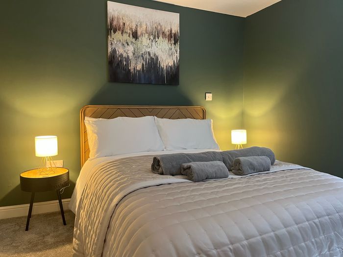 Bedroom with a green painted wall, oak headboard and rolled towels on the bed