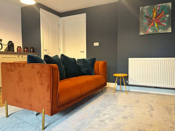 Burnt orange velvet sofa with deep teal cushions below an abstract canvas