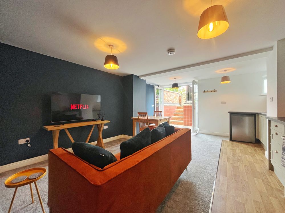 Living area of the lower ground apartment, with a burnt orange sofa and doors onto a private courtyard